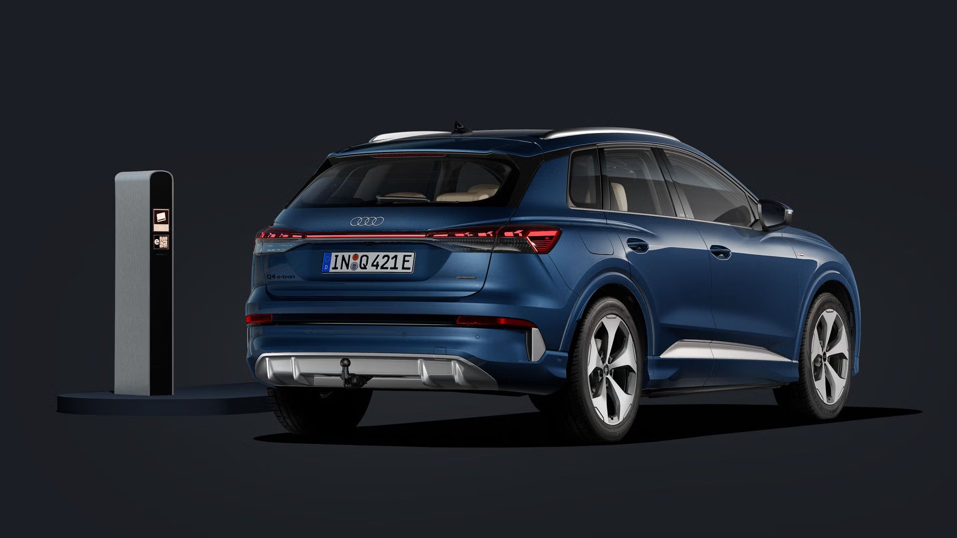 Der Q4 SUV e-tron von schräg hinten auf dunklem Hintergrund, links daneben eine Ladesäule.