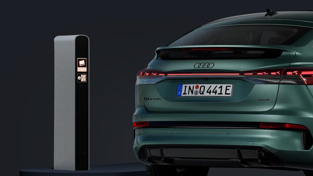 Der Q4 Sportback e-tron von schräg hinten auf dunklem Hintergrund, links daneben eine Ladesäule.
