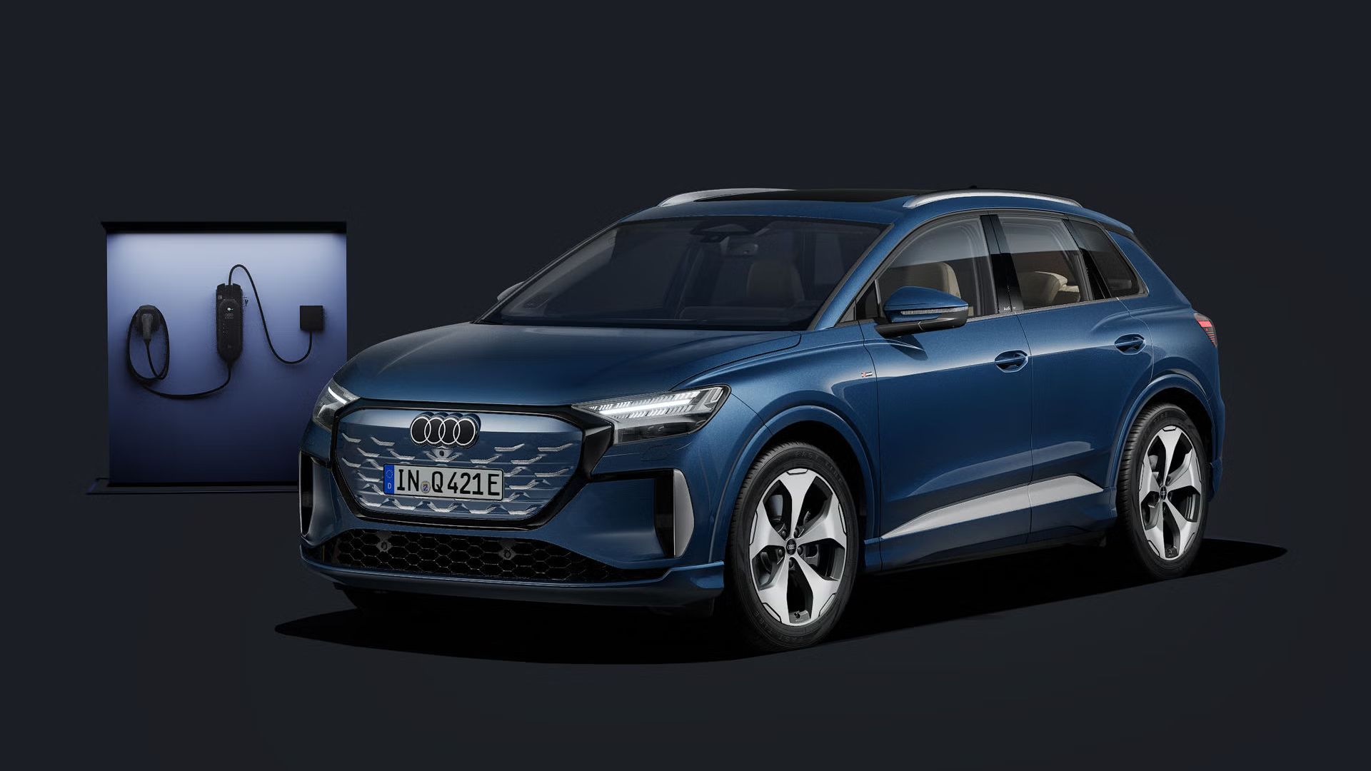 Der Q4 SUV e-tron schräg von vorn auf dunklem Hintergrund, dahinter eine moderne Ladesäule.