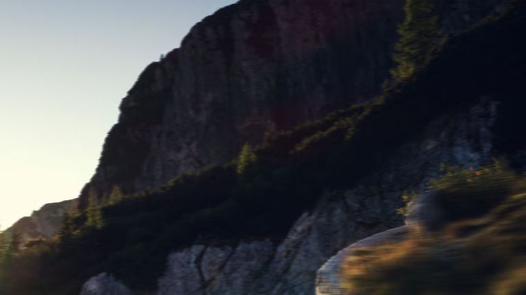 Der Q4 Sportback e-tron bei der Fahrt auf einer Bergstraße. Sonnenstrahlen von links oben beleuchten das Bild, das Fahrzeug wirft Schatten nach vorne.