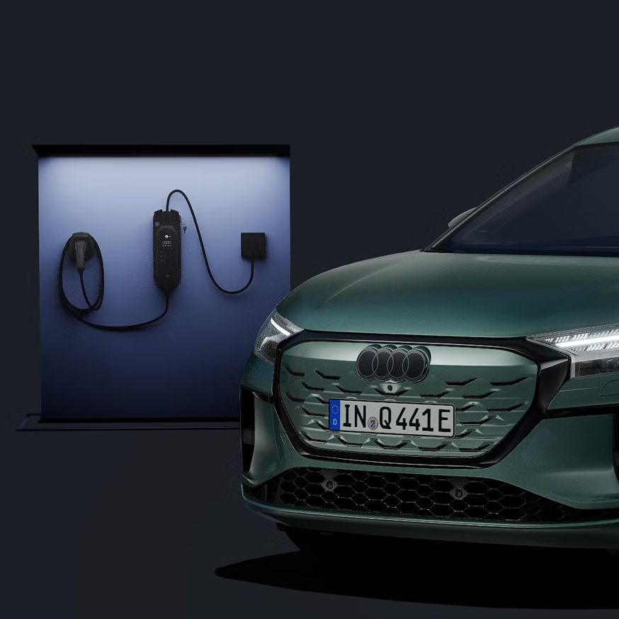 Der Q4 Sportback e-tron schräg von vorn auf dunklem Hintergrund, dahinter eine moderne Ladesäule.